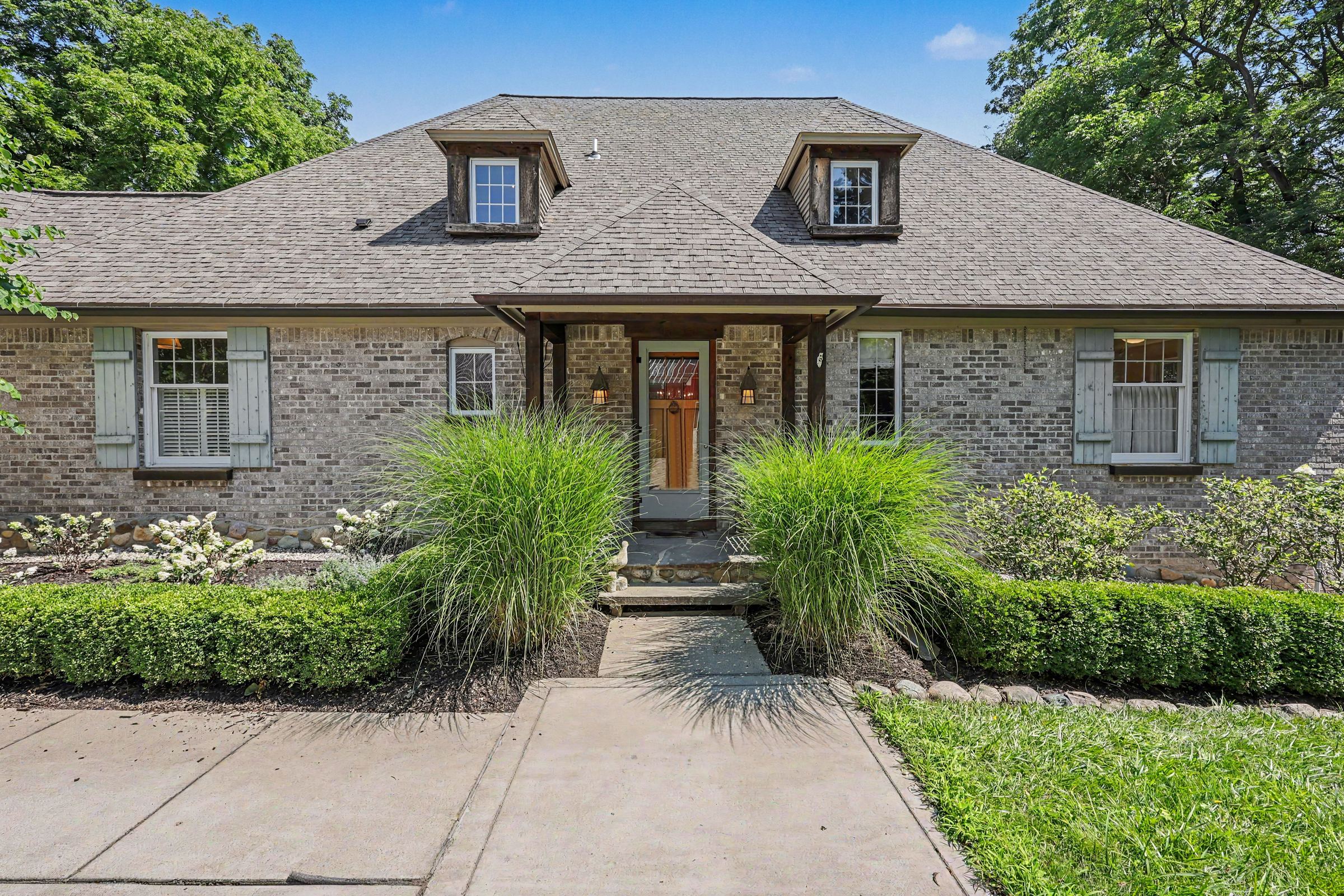 A brick home with blue-gray shutters and tall ornamental grasses along the front walk