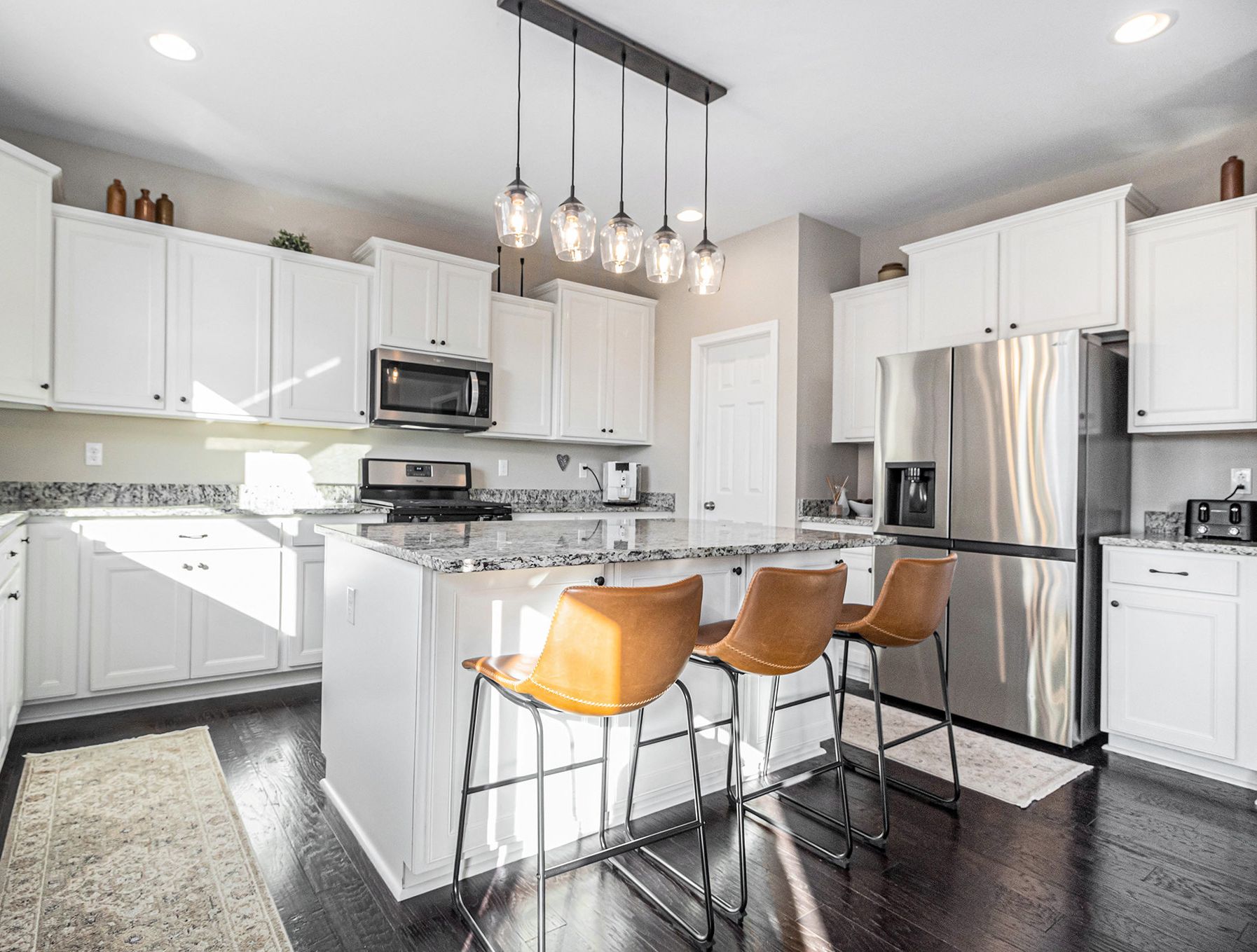 A bright white kitchen with an island, pendant lights and leather bar stools