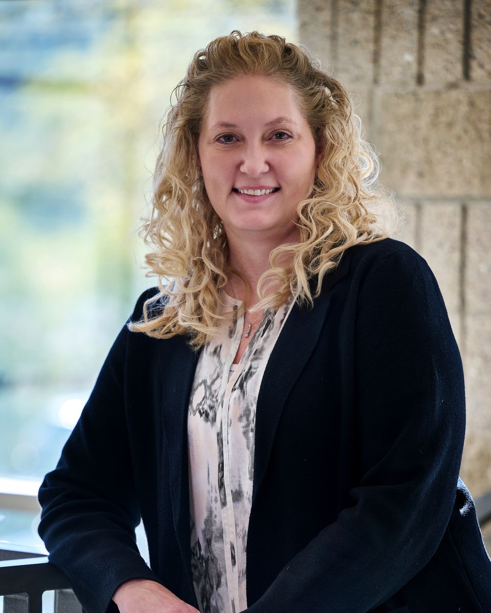 Nancy Arnold smiling, in a navy jacket, leaning on a railing in front of a bright window